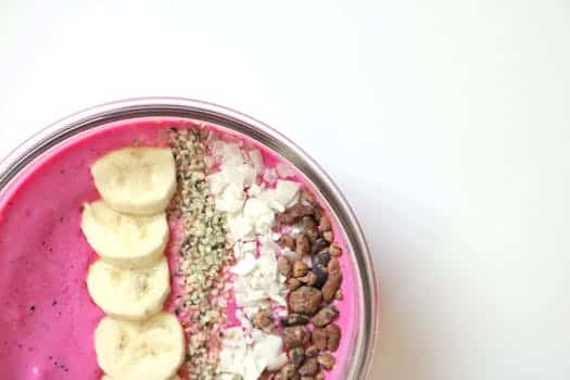 Bright pink smoothie bowl with bananas, seeds, and toppings for a healthy breakfast.