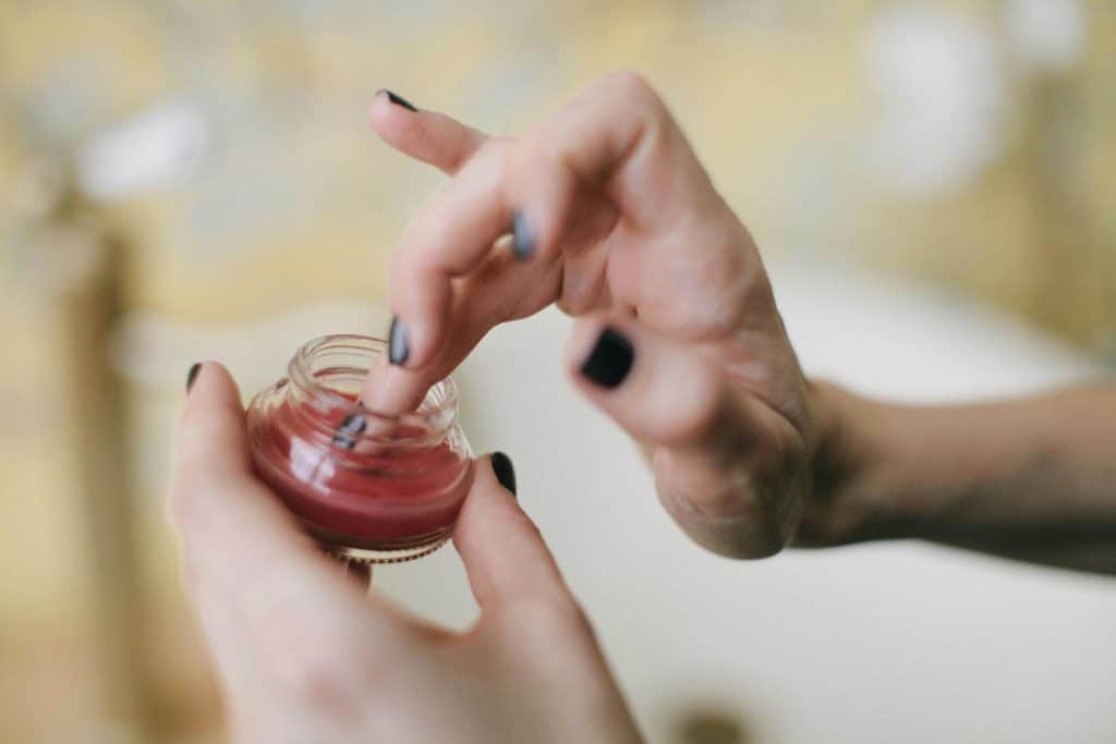 Close-up of a woman applying balm from a glass jar, focusing on skincare aesthetics.