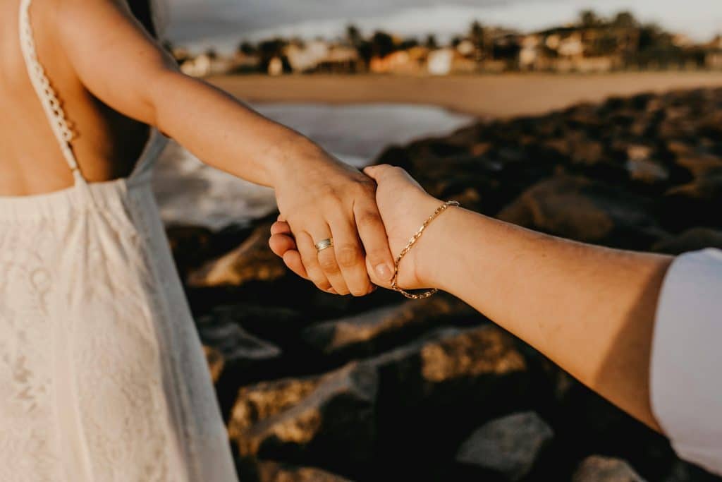 A romantic moment with a couple holding hands on a rocky beach at sunset summer solstice