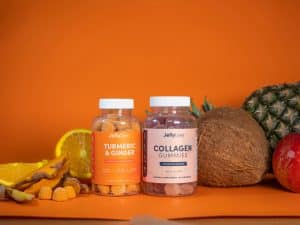 Colorful tropical beauty supplements in gummy form, surrounded by fresh fruits like coconut, pineapple, and orange.