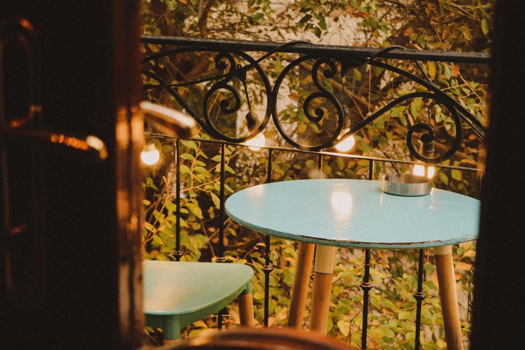 Charming balcony setup with a blue table, chair, and warm lights, inviting a serene evening vibe.