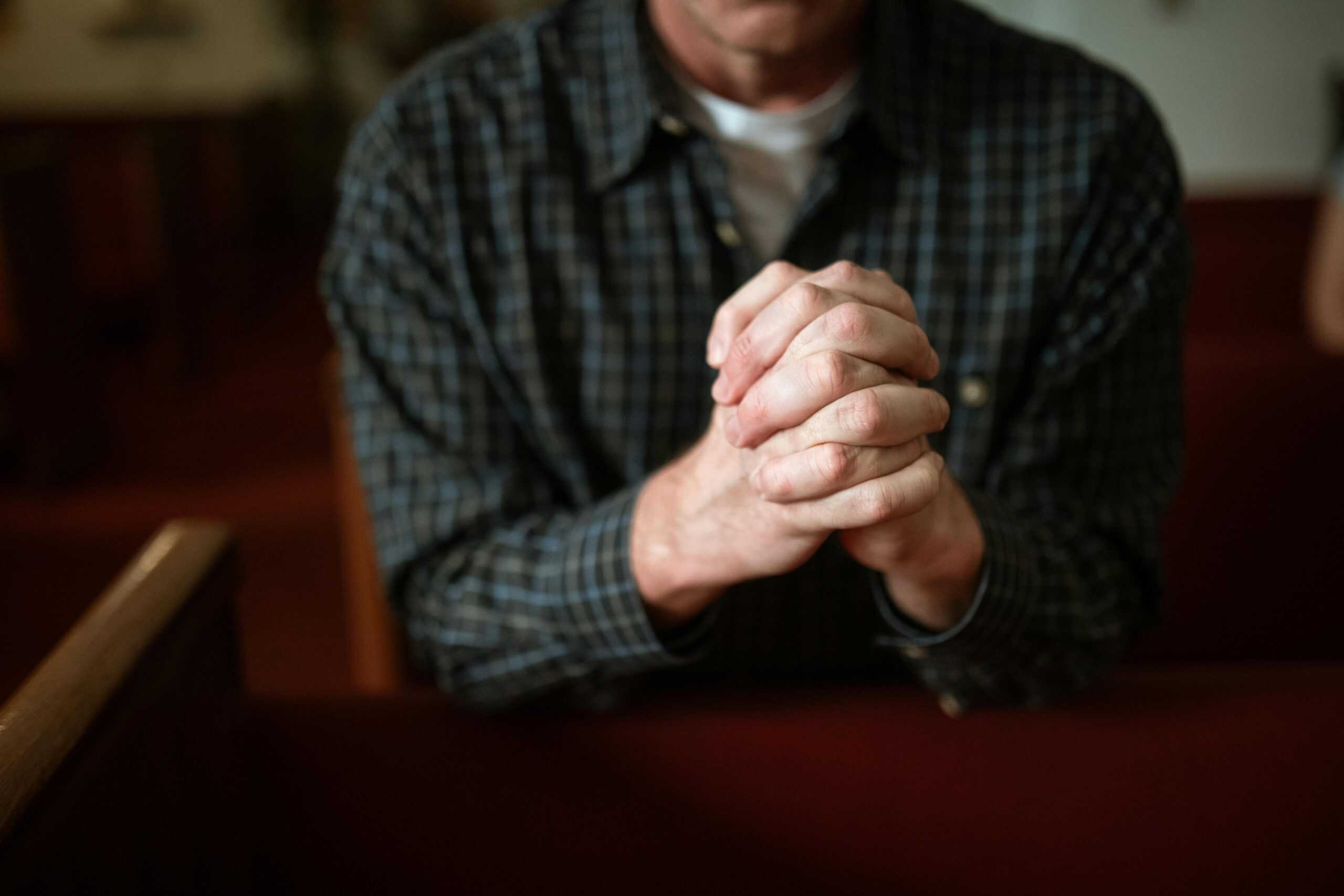 A man in a checked shirt praying in a church, hands clasped together. daily devotion