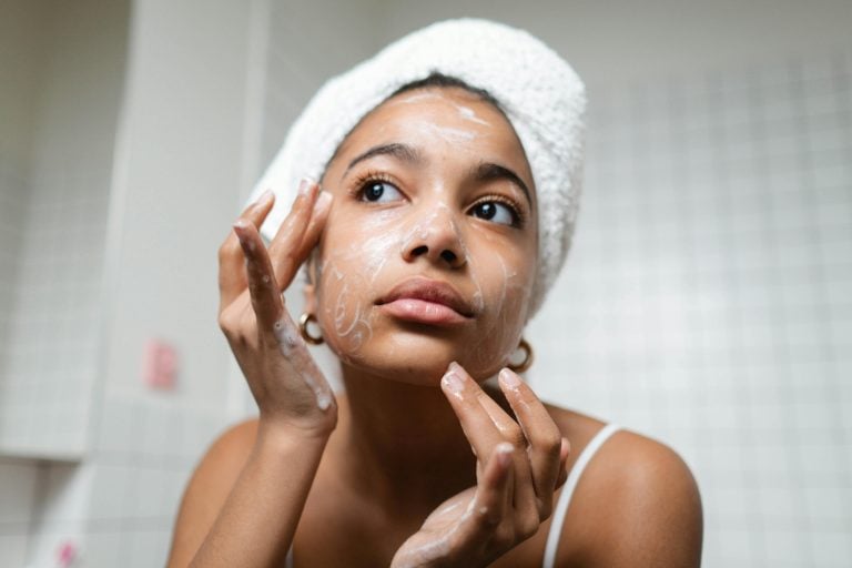 A young woman applies skincare cream in a modern bathroom setting., moisturizers
