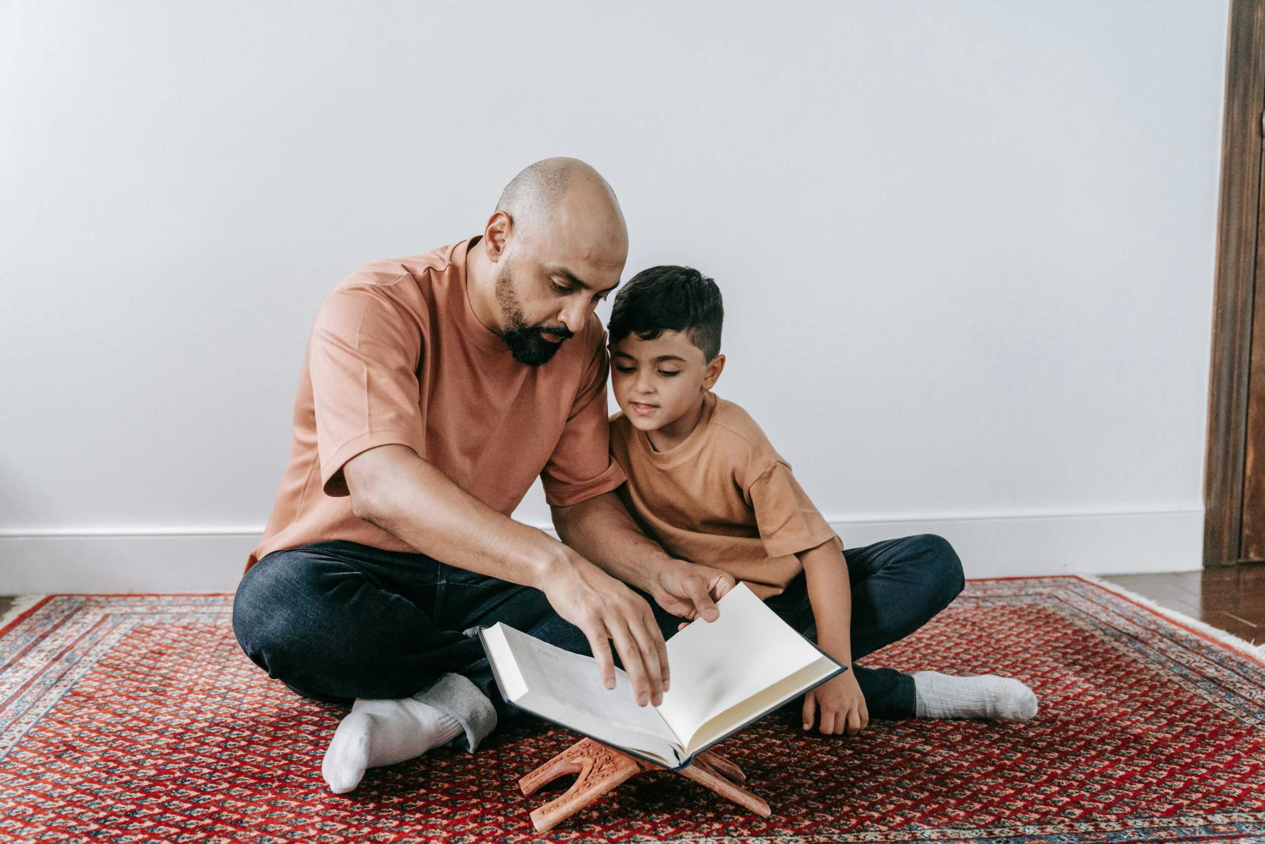 A father and son sitting on a rug, bonding over reading indoors. Proverbs 3