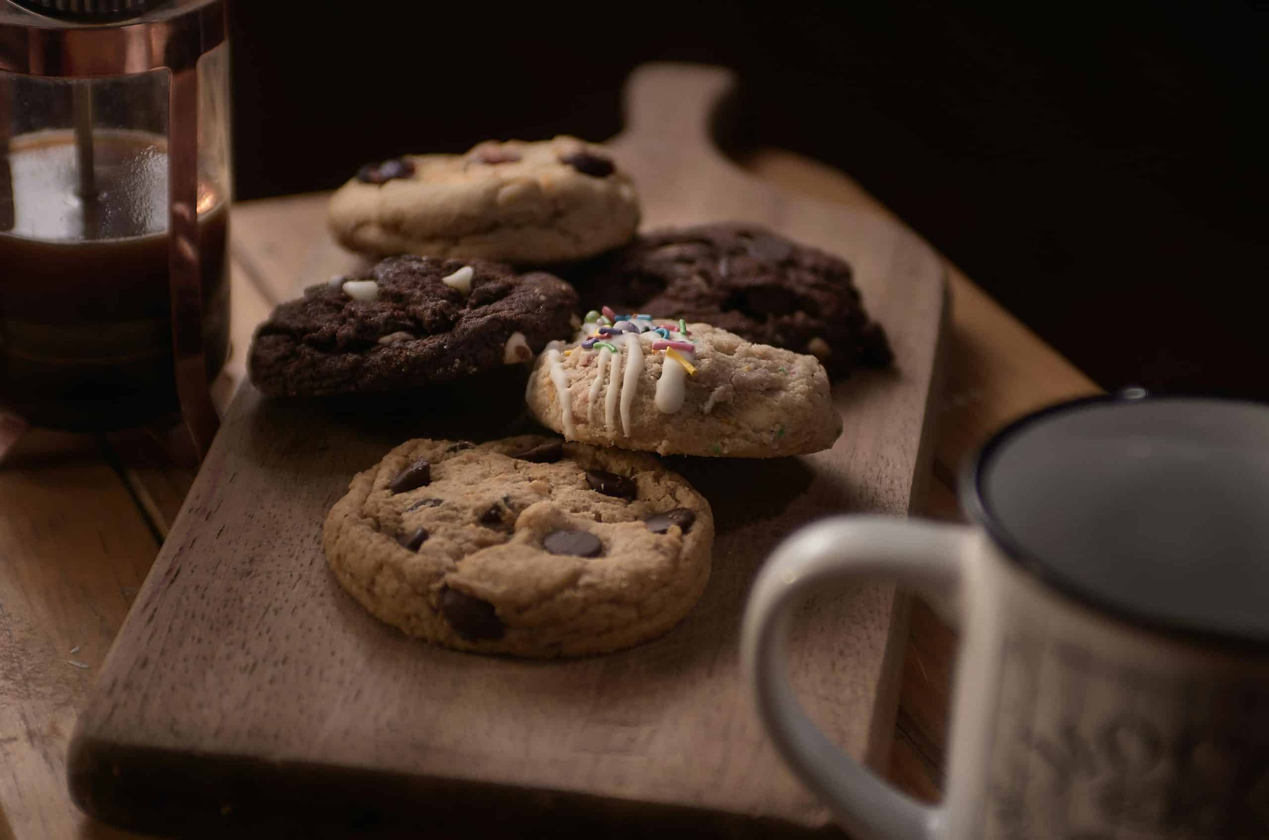 Delicious assorted cookies on a wooden board accompanied by coffee, perfect for a cozy snack time.