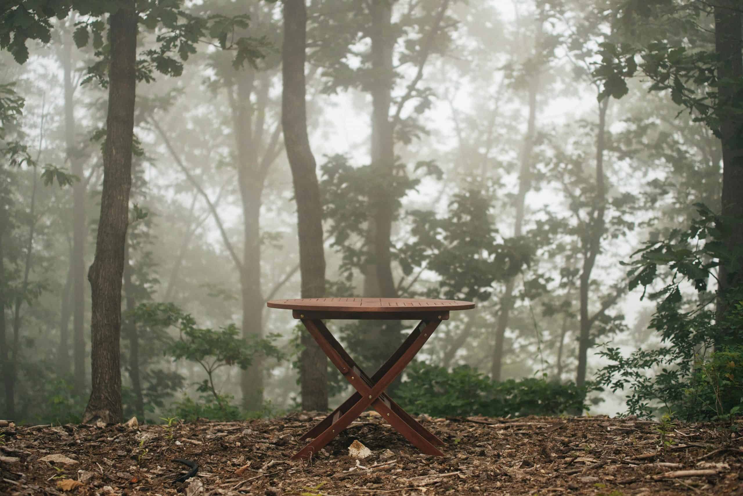 outdoor furniture, winterizing, A wooden table stands alone in a foggy forest, surrounded by dense trees and mist.