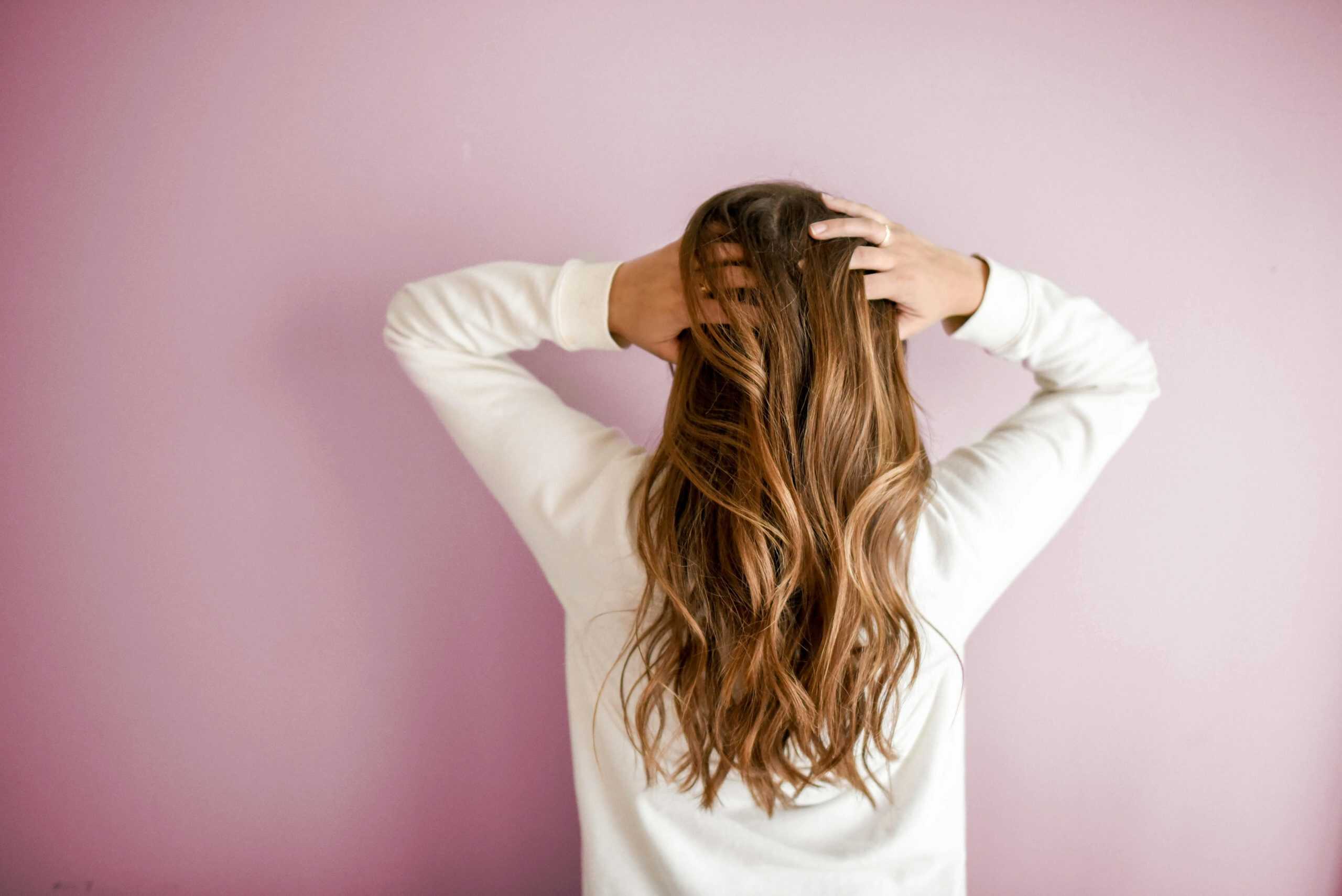 Back view of a woman with elegant long brown hair against a pink wall, showcasing stylish hair design. hair masks