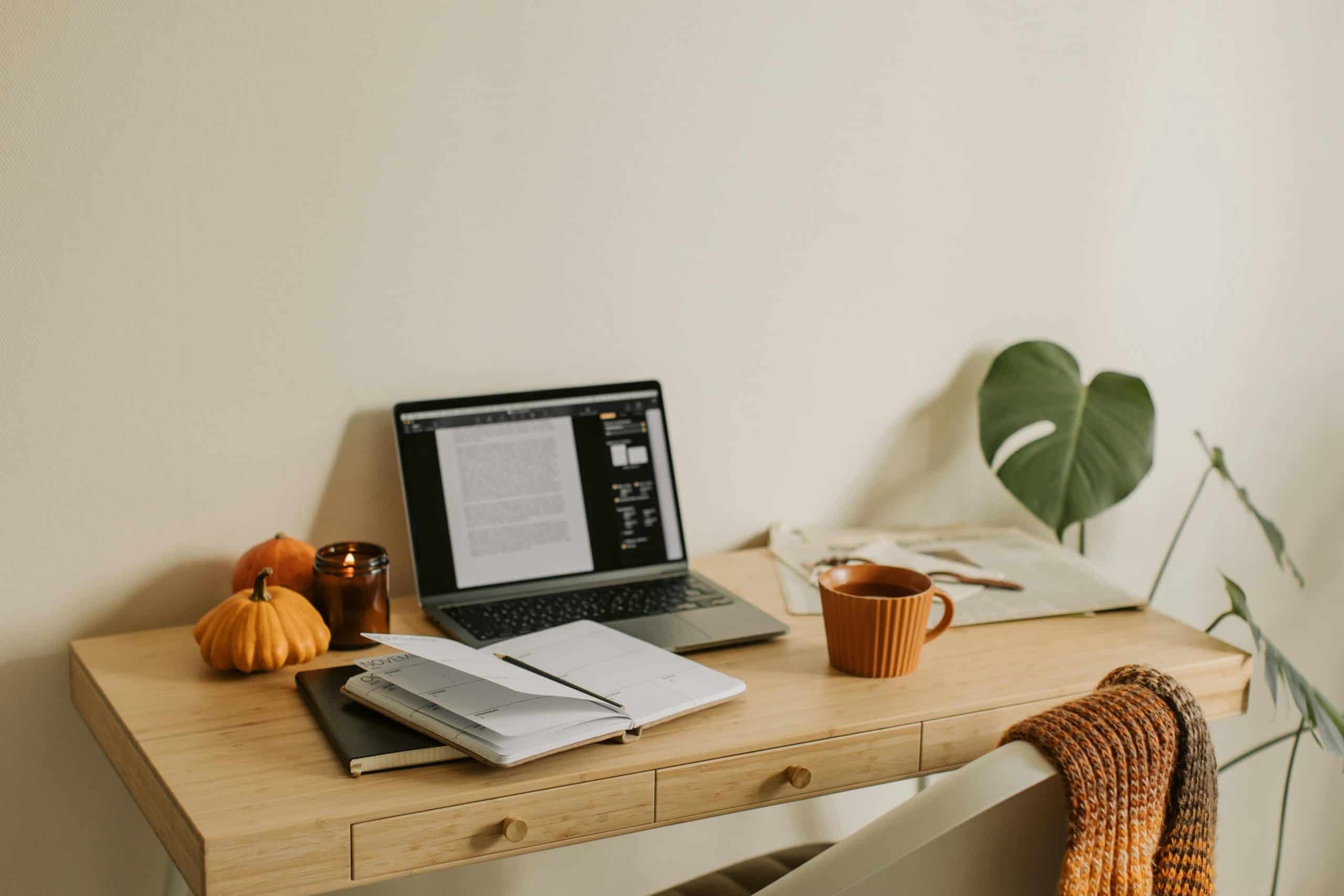 This photograph has a desk, a laptop, and notebooks. Fall dorm decor can provide a cozy studying atmosphere.