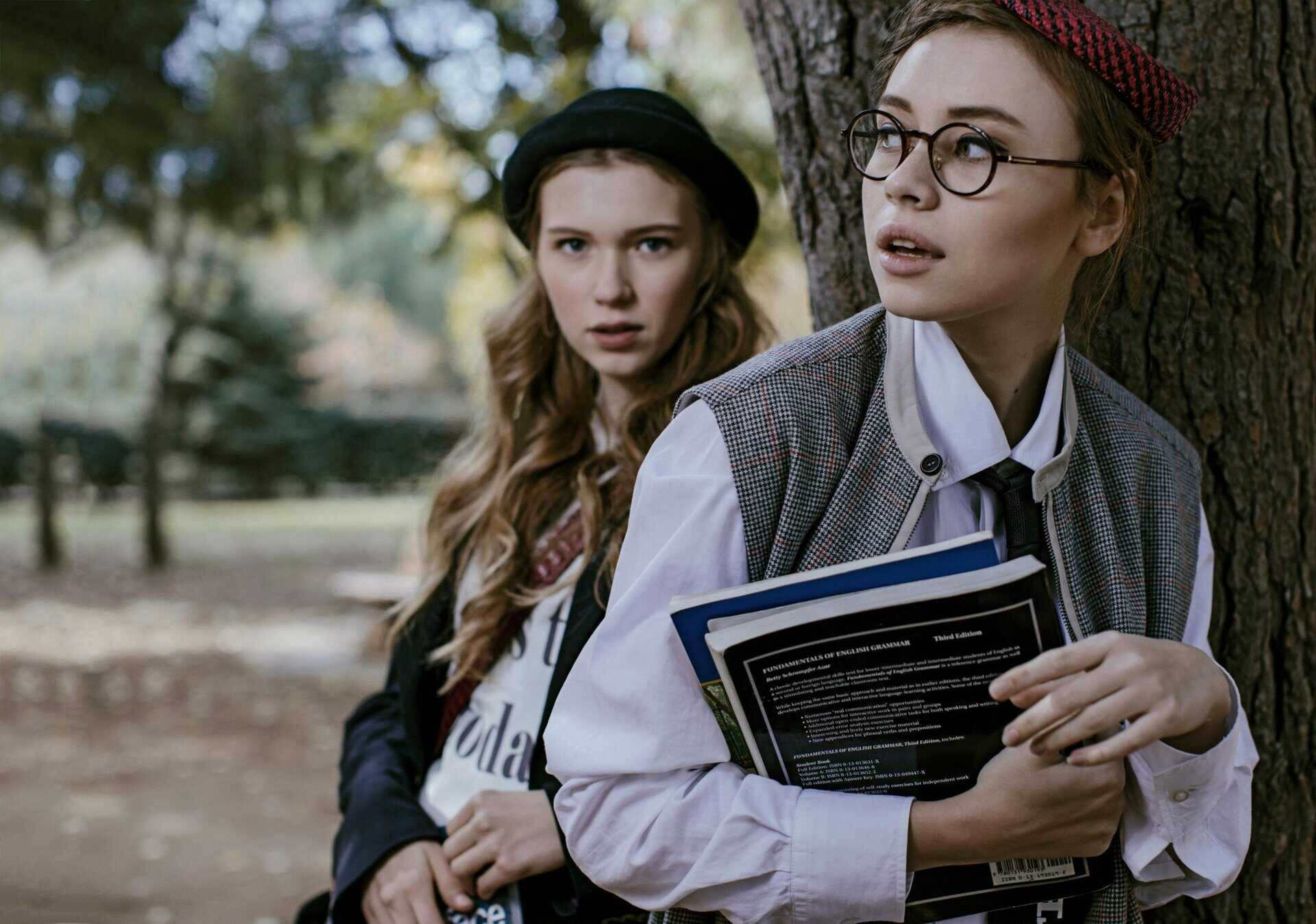 Two stylish young women outdoors, holding books, with a vintage fashion vibe. Fall fashion, fashion trend