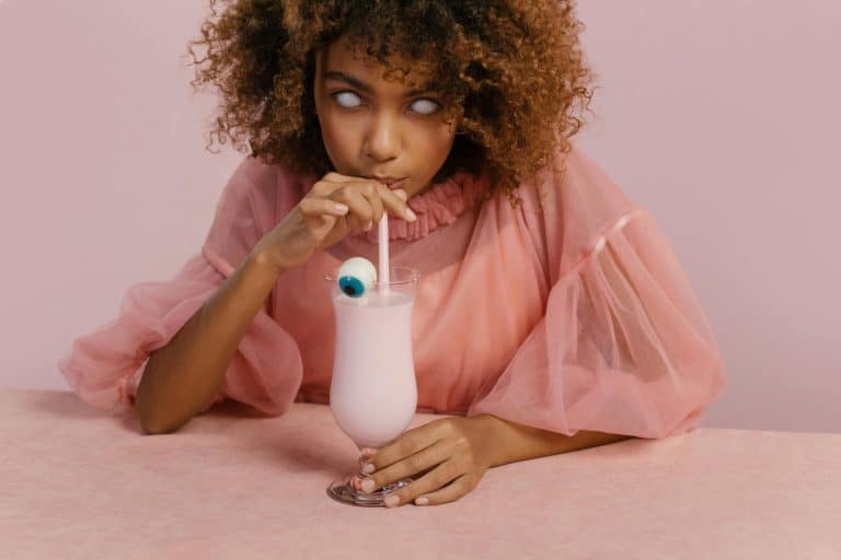 Young woman in a creative Halloween costume sipping a milkshake with a candy eyeball. halloween drinks