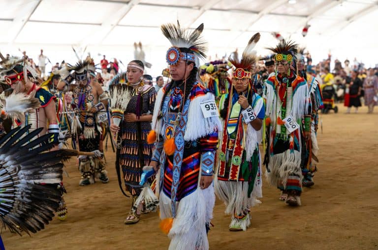 Native American dancers in colorful traditional attire at a vibrant pow wow gathering. Native American Designers